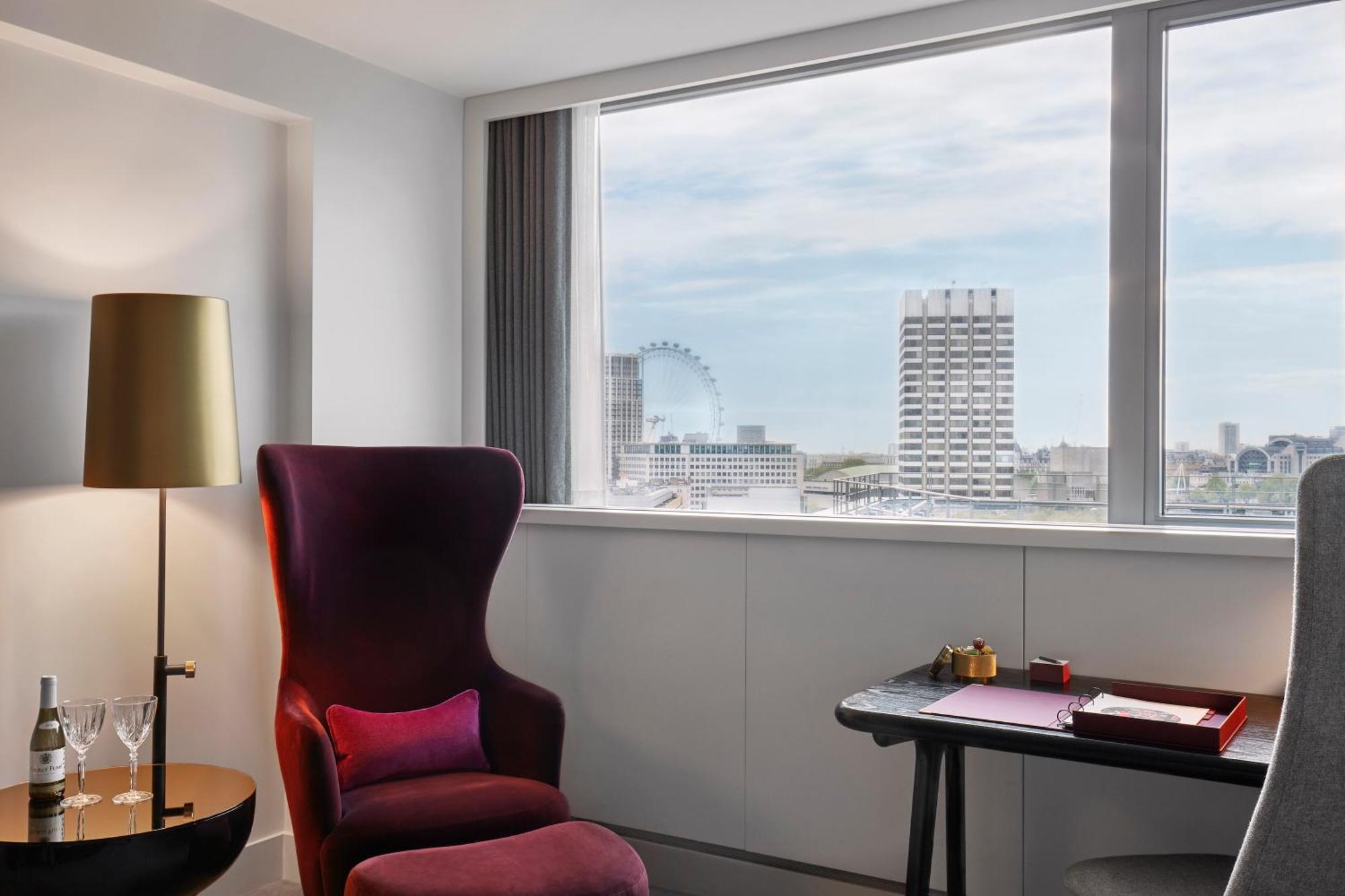 Hotel Sea Containers Londres Exterior foto The photo shows a modern and stylish hotel room featuring a large window with a view of the city skyline. There is a plush, deep purple armchair with a pink cushion in one corner, creating a cozy seating area. Next to the chair, there's a sleek floor