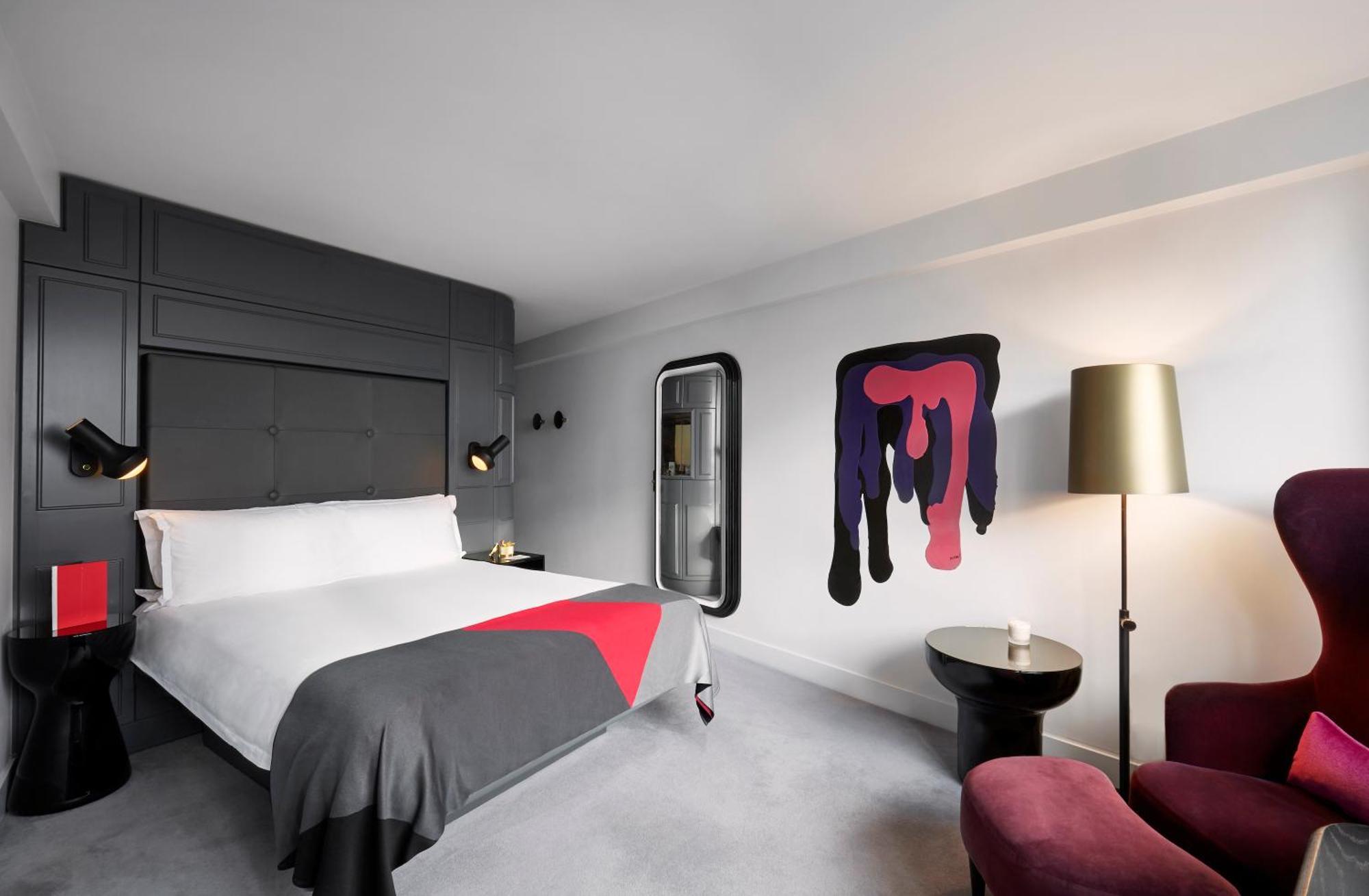 Hotel Sea Containers Londres Exterior foto The photo shows a modern hotel room featuring a large bed with a gray and red blanket. The room has a minimalist design with gray walls, and one wall features an abstract artwork in vibrant colors, including purple and pink. There are two stylish bed