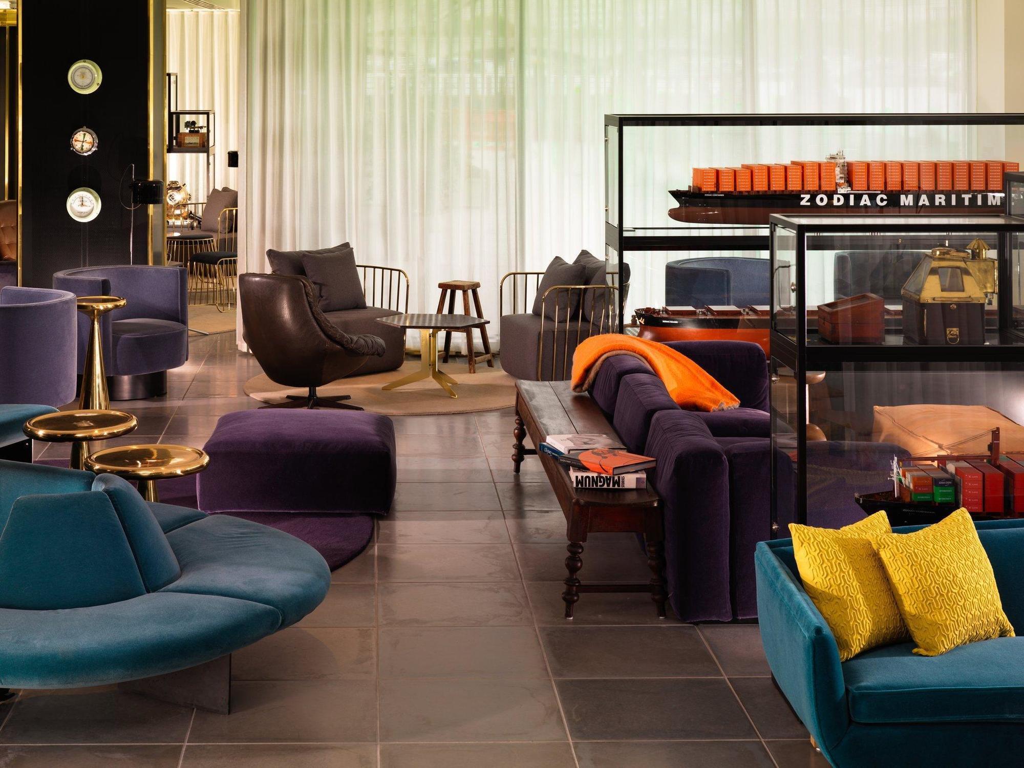 Hotel Sea Containers Londres Exterior foto The photo depicts a modern interior space, likely a lounge or lobby area. The design features a variety of stylish furniture pieces, including a curved blue sofa, purple armchairs, and a sleek black chair. There is a mix of coffee tables and side tab