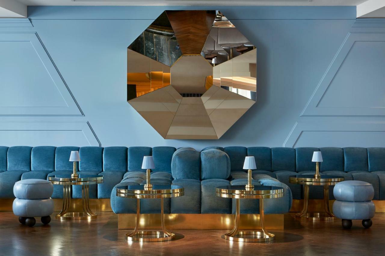 Hotel Sea Containers Londres Exterior foto The photo depicts a stylish and modern interior space. The focal point is a large, octagonal mirror mounted on the wall, which reflects light and adds depth to the room. In front of the mirror, there is a plush, curved sofa in a soft blue hue. The so