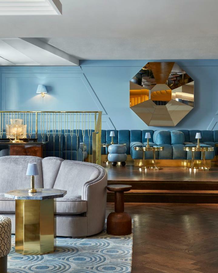 Hotel Sea Containers Londres Exterior foto The photo depicts a stylish lounge area featuring a soft blue color palette. There is a plush sofa in light blue and a series of small tables with brass legs scattered throughout the space. A large, faceted mirror is mounted on the wall, adding a mod