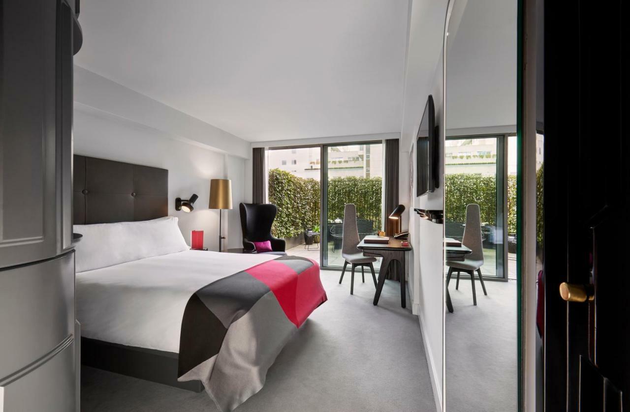 Hotel Sea Containers Londres Exterior foto The photo shows a modern hotel room featuring a large bed with a minimalist design. The bed is adorned with a colorful bedspread, primarily in shades of gray, white, and pink. There are two large windows that provide natural light and overlook a gree