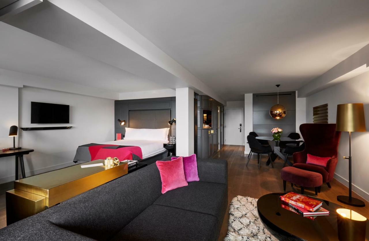 Hotel Sea Containers Londres Exterior foto The photo shows a modern hotel room that features a stylish design. On one side, there is a gray couch with vibrant pink pillows, complemented by a sleek glass coffee table. Across from the couch, a bed with white linens is visible, set against a dar