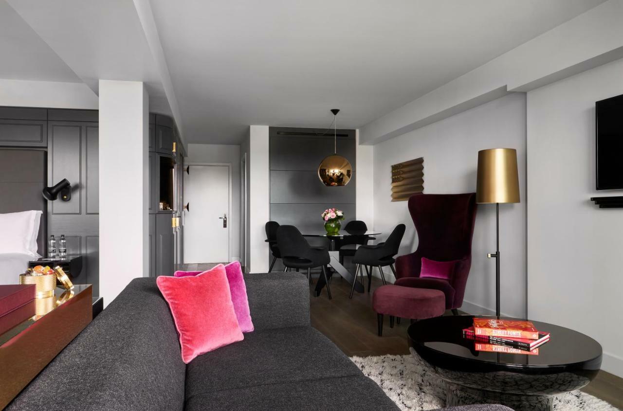 Hotel Sea Containers Londres Exterior foto The photo shows a modern and stylish living space. There is a gray sofa with two pink cushions in the foreground. In the background, there is a dining area with a round black table and black chairs. A decorative pendant light hangs above the table. T
